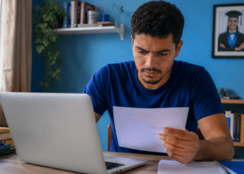 Jovem consulta no notebook o resultado da 2ª chamada do Prouni 2026.2 e analisa um documento com informações da seleção.