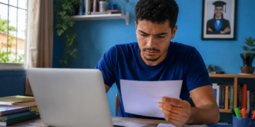 Jovem consulta no notebook o resultado da 2ª chamada do Prouni 2026.2 e analisa um documento com informações da seleção.