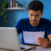 Jovem consulta no notebook o resultado da 2ª chamada do Prouni 2026.2 e analisa um documento com informações da seleção.