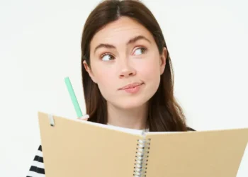 Você escreve “click” ou “clique”? Entenda a diferença e evite erro de português 4 Mulher segurando caderno e caneta com expressão de dúvida.