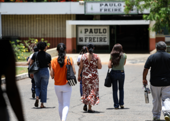 Pessoas caminham em direção a uma escola, representando participantes da Prova Nacional Docente 2026.