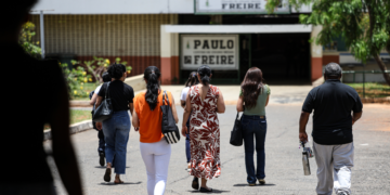 Pessoas caminham em direção a uma escola, representando participantes da Prova Nacional Docente 2026.