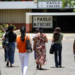 Pessoas caminham em direção a uma escola, representando participantes da Prova Nacional Docente 2026.