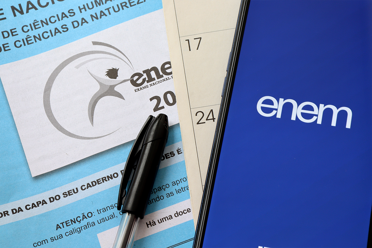 Competências da redação do Enem 2026 Caderno do Enem e celular com aplicativo do exame representando orientações para a redação do Enem 2026.