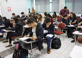 Estudantes sentados em carteiras de uma sala de aula cheia, com cadernos abertos e mochilas no chão, durante atividade de preparação para as provas do Enem 2026.