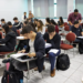 Provas do Enem 2026 se aproximam; MEC reforça orientações para estudantes 10 Estudantes sentados em carteiras de uma sala de aula cheia, com cadernos abertos e mochilas no chão, durante atividade de preparação para as provas do Enem 2026.