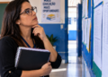 Professora consulta quadro de avisos representando a divulgação do gabarito e resultado da PND 2026.