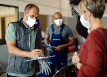 Curso online de Vigilância Sanitária ensina sobre fiscalização e controle de qualidade; veja como participar 5 Homem de máscara faz anotações em uma prancheta ao lado de duas pessoas em uma oficina mecânica.