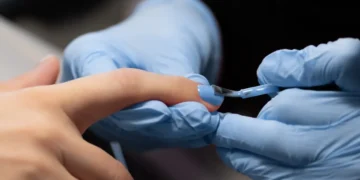 Profissional aplica esmalte azul em unha durante procedimento de alongamento e cuidados de manicure.