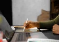 Muito além de criar imagens: curso de Design Gráfico aborda conhecimentos para desenvolver projetos visuais 13 Pessoa utiliza caneta digital em tablet gráfico ao lado de notebook, representando o aprendizado de Design Gráfico e a criação de projetos visuais.
