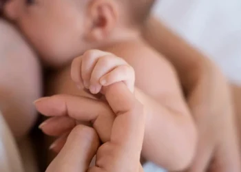 Curso de Aleitamento Materno ensina cuidados essenciais com a amamentação e oferece certificado; veja como participar 6 Bebê durante a amamentação segura a mão da mãe em imagem sobre curso de aleitamento materno.