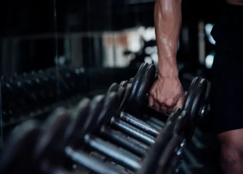 Curso de Musculação: aprenda sobre exercícios, técnicas de treinamento e cuidados durante a prática 5 Pessoa segurando halter em academia, representando exercícios de musculação, treinamento de força e técnicas para desenvolvimento muscular.