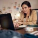 Curso online de Vendas B2B ensina estratégias para conquistar clientes e melhorar negociações 11 Mulher utiliza notebook em um ateliê, com tecidos e materiais de costura sobre a mesa.