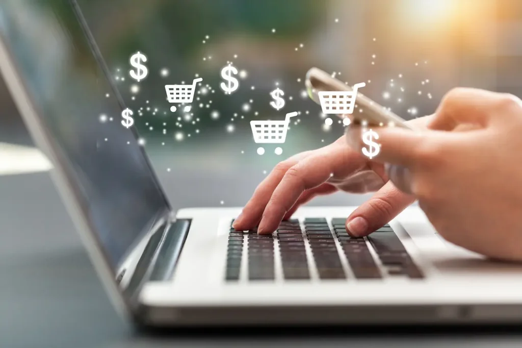 Pessoa utiliza notebook e celular em ambiente de compras online, representando curso de atendimento e vendas no varejo.