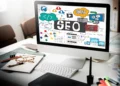 Computador com a palavra SEO na tela e ilustrações de estratégias digitais, marketing de conteúdo e otimização de sites.