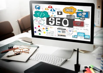 Computador com a palavra SEO na tela e ilustrações de estratégias digitais, marketing de conteúdo e otimização de sites.