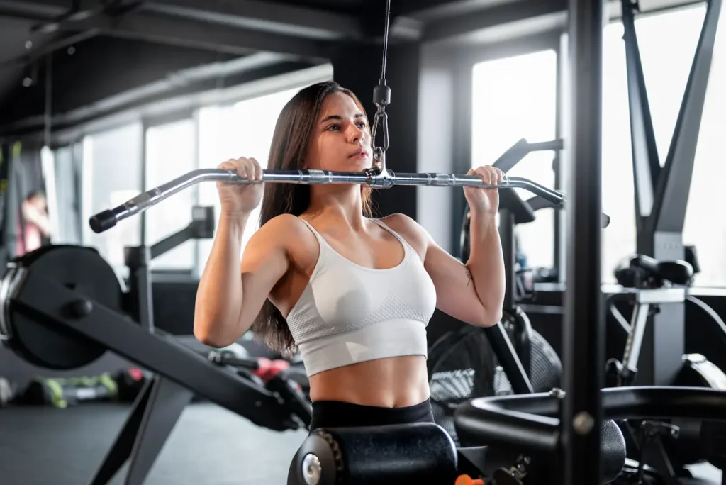 Mulher realizando exercício de puxada na polia alta em academia, ilustrando técnicas de musculação e treinamento de força.