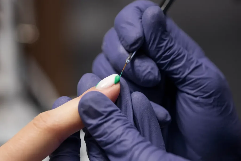 Nail designer realiza técnica de decoração e acabamento em unha durante procedimento profissional.